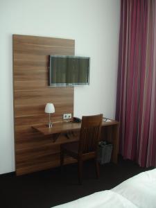 Schlafzimmer mit einem Schreibtisch und einem TV an der Wand in der Unterkunft Hotel Sentio in Vöhringen