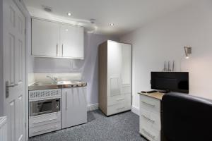 uma pequena cozinha com armários brancos e uma televisão em Old County Court em Coventry