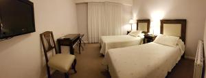 a hotel room with two beds and a desk and a television at Hotel Kapenke in El Calafate
