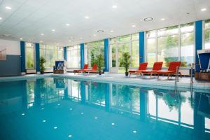 a swimming pool with red chairs and a large room with windows at Mercure Stuttgart Sindelfingen an der Messe in Sindelfingen