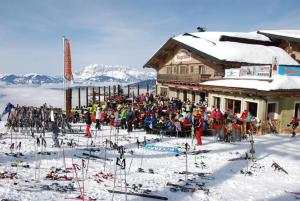 una multitud de personas de pie en frente de una cabaña de esquí en Gasthof Kogelalm en Wagrain