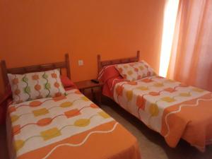 2 camas en una habitación con paredes de color naranja en Pensión Restaurante Páramo, en La Herradura