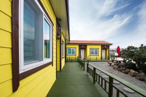 a yellow building with a porch with a window at Brassica Flower Pension in Seogwipo
