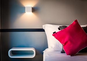 a bed with a red pillow and a light on the wall at Teku Sardinia Boutique Hotel in Bari Sardo
