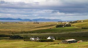 a green field with houses and animals in the distance at Buaile nan Carn in Kilmuir