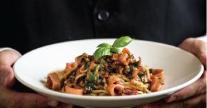 a person holding a white bowl of pasta with a basil leaf on top at Penn's View Hotel Philadelphia in Philadelphia