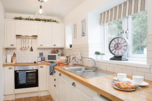 uma cozinha com armários brancos, um lavatório e uma janela em Mona's Cottage em Berwick-Upon-Tweed