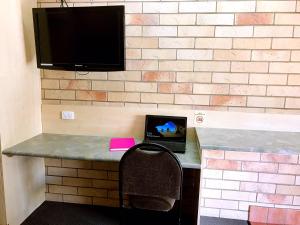 a desk with a laptop and a tv on a brick wall at Starlight Motor Inn in Roma