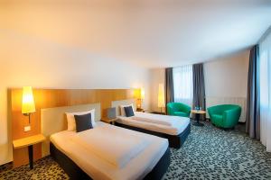 a hotel room with two beds and green chairs at ACHAT Hotel Offenbach Plaza in Offenbach