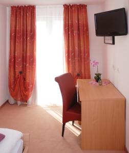 a room with a desk with a chair and a television at Hotel Ackermann in Riedstadt