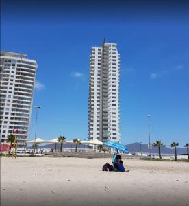 dos personas sentadas bajo un paraguas en la playa en Departamento Costa Mansa, en Coquimbo