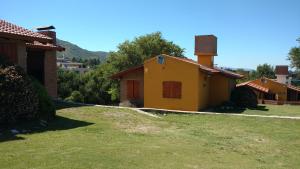 ein kleines gelbes Haus in einem Hof neben einem Gebäude in der Unterkunft Cabañas Los Gauchitos in La Falda