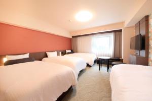 a hotel room with three beds and a television at Richmond Hotel Naha Kumoji in Naha