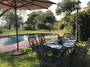 una mesa con sillas y una sombrilla junto a la piscina en Cuckoos Nest Guest House, en Louis Trichardt