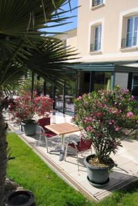 a picnic table and chairs in a courtyard with pink flowers at Brit Hotel Châteaudun in Châteaudun