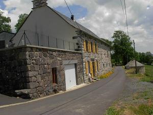 a stone building with yellow shuttered windows on a road at Vacances au pied des Monts du Cantal in Laveissière