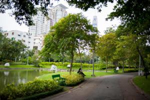 曼谷的住宿－勝利公園旅舍，坐在带池塘的公园长凳上的人