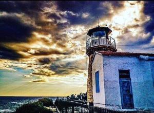 a lighthouse on the ocean with a cloudy sky at Villa Galleria in Perivolia