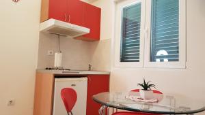 a small kitchen with red cabinets and a glass table at Apartments TM in Bijela