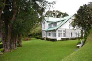 uma casa branca com um telhado verde e um quintal em Brockenhurst Bungalow em Nuwara Eliya