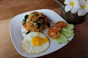 a plate of food with noodles and an egg and tomatoes at Semarandana Bedrooms and Pool in Sanur