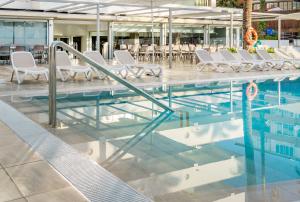 a swimming pool with white chairs and tables at Globales Panamá in Palmanova