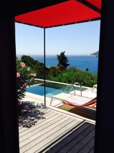 une terrasse avec un parasol rouge et une piscine dans l'établissement Villa Mirabel, sur l'Île du Levant