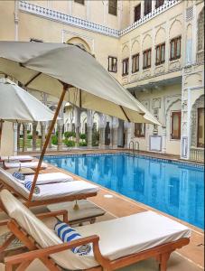 uma piscina com cadeiras e guarda-sóis num edifício em The Raj Palace (Small Luxury Hotels of the World) em Jaipur