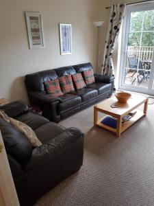 a living room with a black leather couch and a coffee table at Apartment 3, Pheonix Flats. in Portree