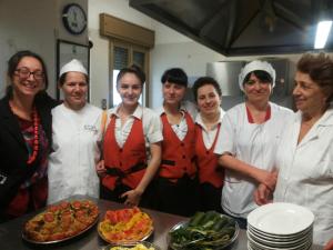 a group of people standing in a kitchen with food at Albergo Stella in Tolè