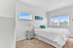 a white bedroom with a bed and two windows at The Little Blue Bach in Oneroa Village by Waiheke Unlimited in Oneroa