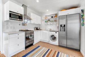 a kitchen with white cabinets and a stainless steel refrigerator at The Little Blue Bach in Oneroa Village by Waiheke Unlimited in Oneroa