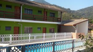 a green building with a white fence and a swimming pool at Montanhas Bem Te Vi in Caraguatatuba