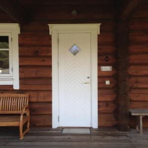 eine weiße Tür auf einem Holzhaus mit einer Bank in der Unterkunft Vila Migla in Pašekščiai
