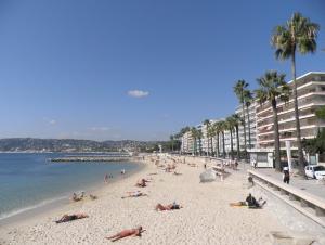 a beach with people laying on the sand and the water at Juan Plage in Juan-les-Pins