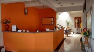 um saguão com uma parede laranja e um bar em Shalon Hotel em Uberaba