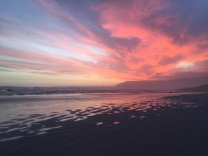 een zonsondergang op een strand met een bewolkte hemel bij Mosselberg on Grotto Beach in Hermanus