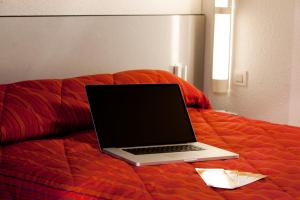 un ordenador portátil sentado en la parte superior de una cama en Premiere Classe Avallon, en Sauvigny-le-Bois