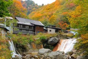 a building next to a waterfall next to a river at Namegawaonsen Fukushimaya in Yonezawa