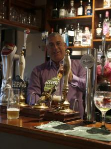 un hombre mayor sentado en un bar con un camarero en The Plough Inn en Little Dewchurch