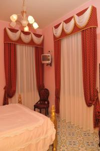 Schlafzimmer mit roten Vorhängen, einem Bett und einem Stuhl in der Unterkunft Albergo Roses in Paola