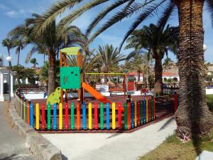une aire de jeux avec une clôture colorée dans un parc planté de palmiers dans l'établissement Maspalomas Experience Holiday House, à Maspalomas
