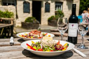 dois pratos de comida numa mesa de madeira com copos de vinho em The Old Inn em Mullion