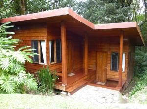 uma cabana de madeira com um alpendre na floresta em Arco Iris Lodge em Monteverde