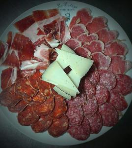 un plato de carne y queso en una mesa en Hostal Rural La Casa Verde, en Cheles