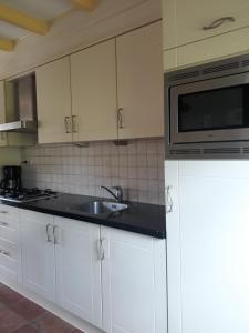 a kitchen with white cabinets and a sink and a microwave at Vakantiewoning de Boshoorn in Serooskerke