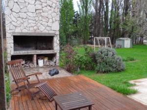 een houten terras met 2 stoelen en een stenen open haard bij Las Acacias in Plottier