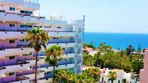 ein hohes weißes Gebäude mit Palmen und dem Meer in der Unterkunft Playa de Las Americas Sea Views in Playa de las Americas
