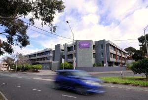 Une voiture bleue descend dans une rue en face d'un bâtiment dans l'établissement Mercure North Melbourne, à Melbourne