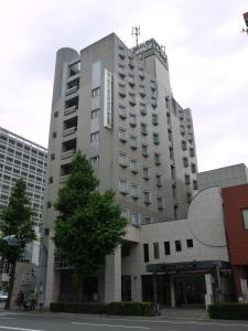 een hoog gebouw met een boom ervoor bij Hotel Route-Inn Hakata Ekiminami in Fukuoka